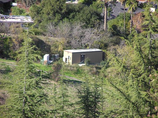 16 - Equipment Shelter and Pad for Our Little Friend
This is the first good shot I've been able to take of the equipment building for our little friend. It's a long shot, taken with a telephoto lens, but you can clearly see the equipment building for the original carrier, and the pad-mounted equipment for the new carrier (on the trunk).   Photograph 04 in this gallery shows the relative positions of the equipment building and our little tree.
